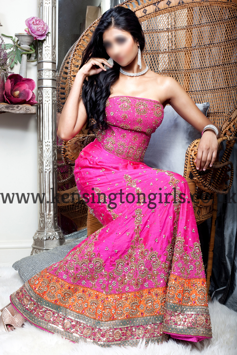 Ria dressed in a full Indian pink exotic gown as she sits on a white chair.